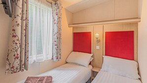 A double room with two beds, a window with sheer curtains, a wall-mounted light, and a wooden headboard.