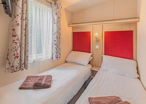 Habitación doble con dos camas, una ventana con cortinas traslúcidas, una lámpara fijada a la pared y un cabecero de madera.