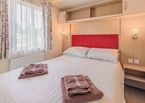 Habitación de hotel con cama, dos lámparas de noche, cabecera roja, ventana con cortinas florales y radiador.