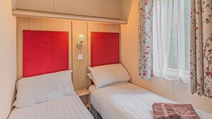 A hotel room with two beds, a wooden headboard, a nightstand, and a window with floral curtains.