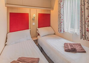 Habitación de hotel con dos camas, cabecero de madera, mesita de noche y ventana con cortinas florales.