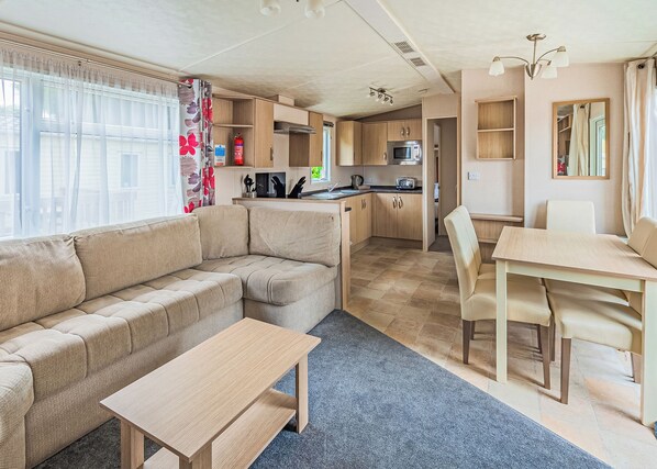 Un espacio habitable compacto con sofá, mesa de comedor, kitchenette y una pequeña zona de cocina.