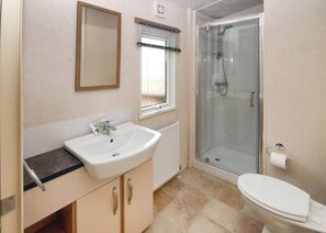 A bathroom with a sink, mirror, window, shower, and toilet. - The Firs are our standard three bedroom mini-lodges. (Dawlish)