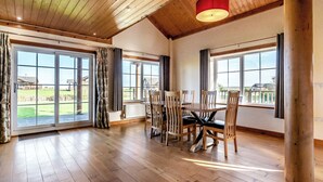 A spacious room with a wooden ceiling, large windows, a dining table with chairs, and a view of a green landscape. - Outstanding, spacious and contemporary two storey lodge. (Hornsea)