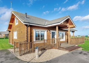 A log cabin with a porch, a chimney, and a gravel driveway.