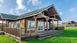 A log cabin with a porch, large windows, and a grassy yard. - Outstanding, spacious and contemporary two storey lodge. (Hornsea)
