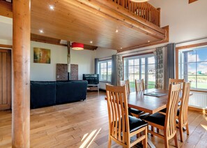 Un vaste espace de vie doté d’un plancher en bois, d’un canapé noir, d’une table à manger avec des chaises en bois et d’une grande fenêtre offrant une vue sur l’extérieur.