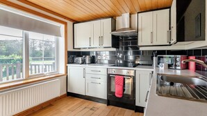 A modern kitchen with wooden ceiling, white cabinets, stainless steel appliances, and a large window. - Outstanding, spacious and contemporary two storey lodge. (Hornsea)