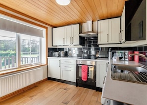 A modern kitchen with wooden ceiling, white cabinets, stainless steel appliances, and a large window.