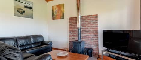 A living room with a black leather sofa, a wooden coffee table, a TV, and a brick fireplace.