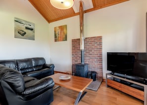 A living room with a black leather sofa, a wooden coffee table, a TV, and a brick fireplace.
