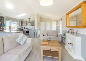 A modern open-plan living area with a kitchen, a sofa, a coffee table, and a fireplace. - Luxury 1 bedroom lodge. (Swinethorpe, Nr Lincoln)