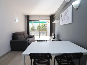 A modern room with a white table and four black chairs, a grey sofa, and a large window with a view of palm trees.