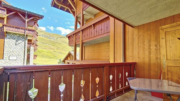 Uma varanda de madeira com uma mesa de metal, uma parede de pedra com uma placa, e vista para as montanhas.