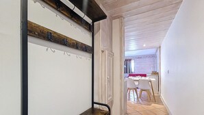 Um corredor com um banco de madeira, um aparador de casacos e uma sala de jantar ao fundo.