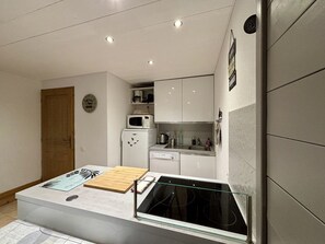Une cuisine compacte dotée d’un îlot central, de meubles blancs et d’un four à micro-ondes placé au-dessus du plan de travail.