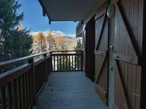 Une terrasse en bois offrant une vue sur des montagnes enneigées et des arbres aux couleurs automnales.