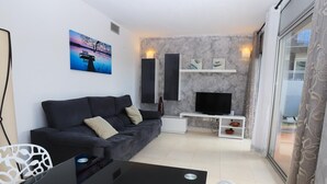 En moderne stue med en sort sofa, et fladskærms-TV og et spisebord.