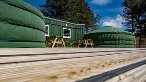 A wooden deck with a view of a green building and large green tents.