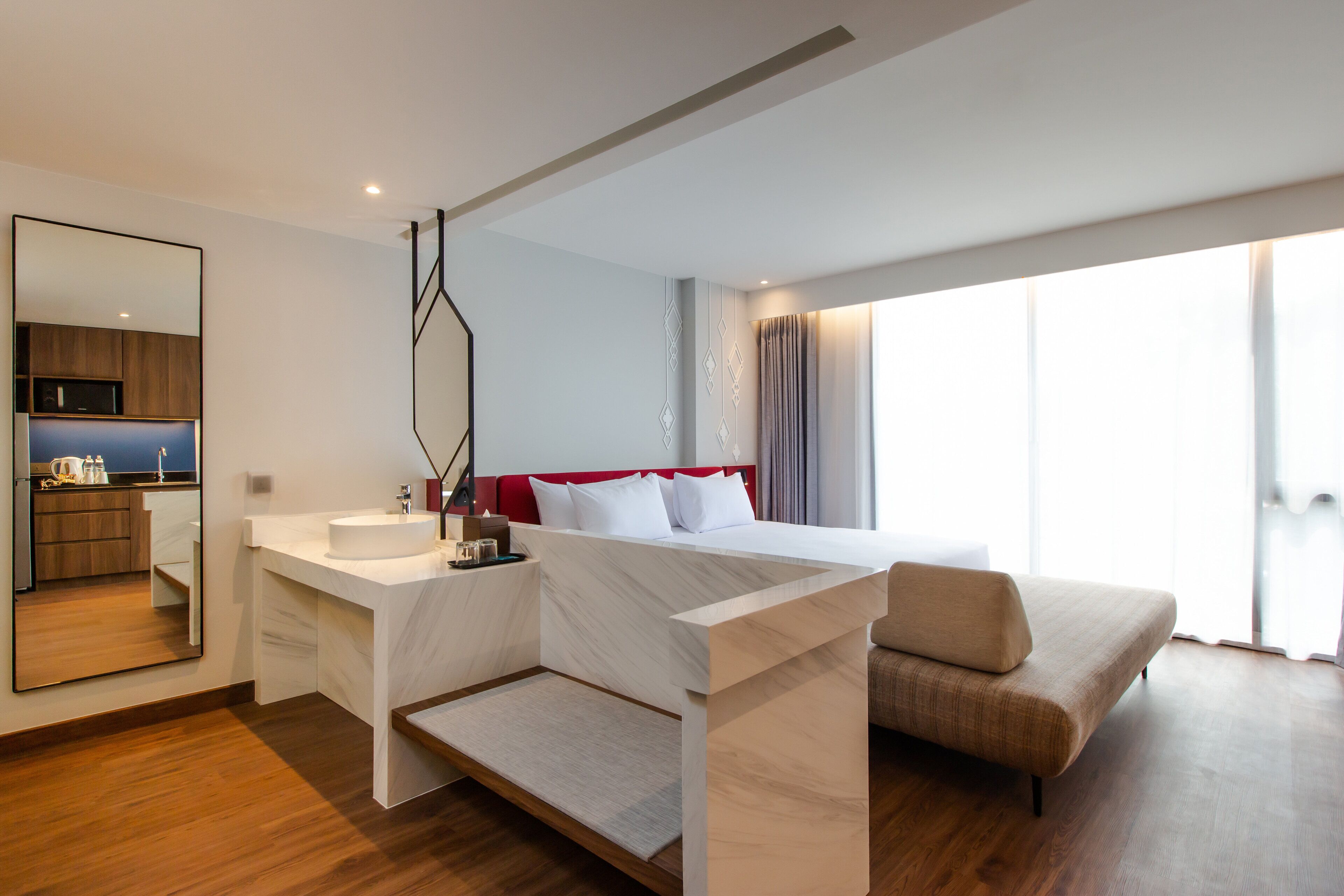 Een moderne hotelkamer met een bed, een bank, een badkamer met een wastafel en een groot raam.