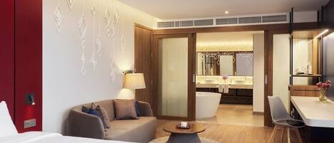 Habitación de hotel con cama, sofá, mesa de comedor y baño visible a través de una puerta abierta.
