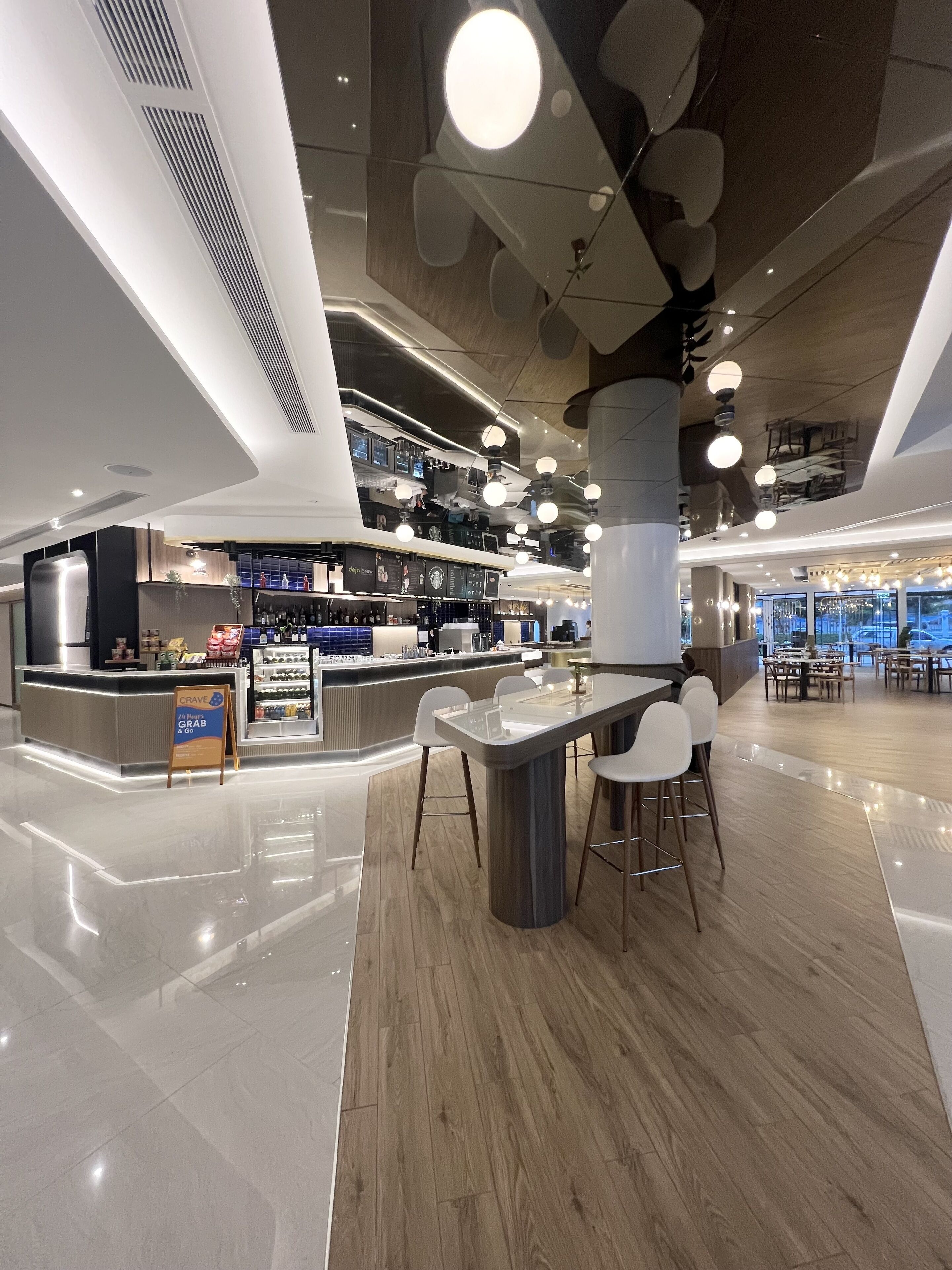 Ein modernes Interieur mit einer zentralen Bar, Sitzgelegenheiten und einem sichtbaren Schild für 'CRAVE GRAB & GO'.