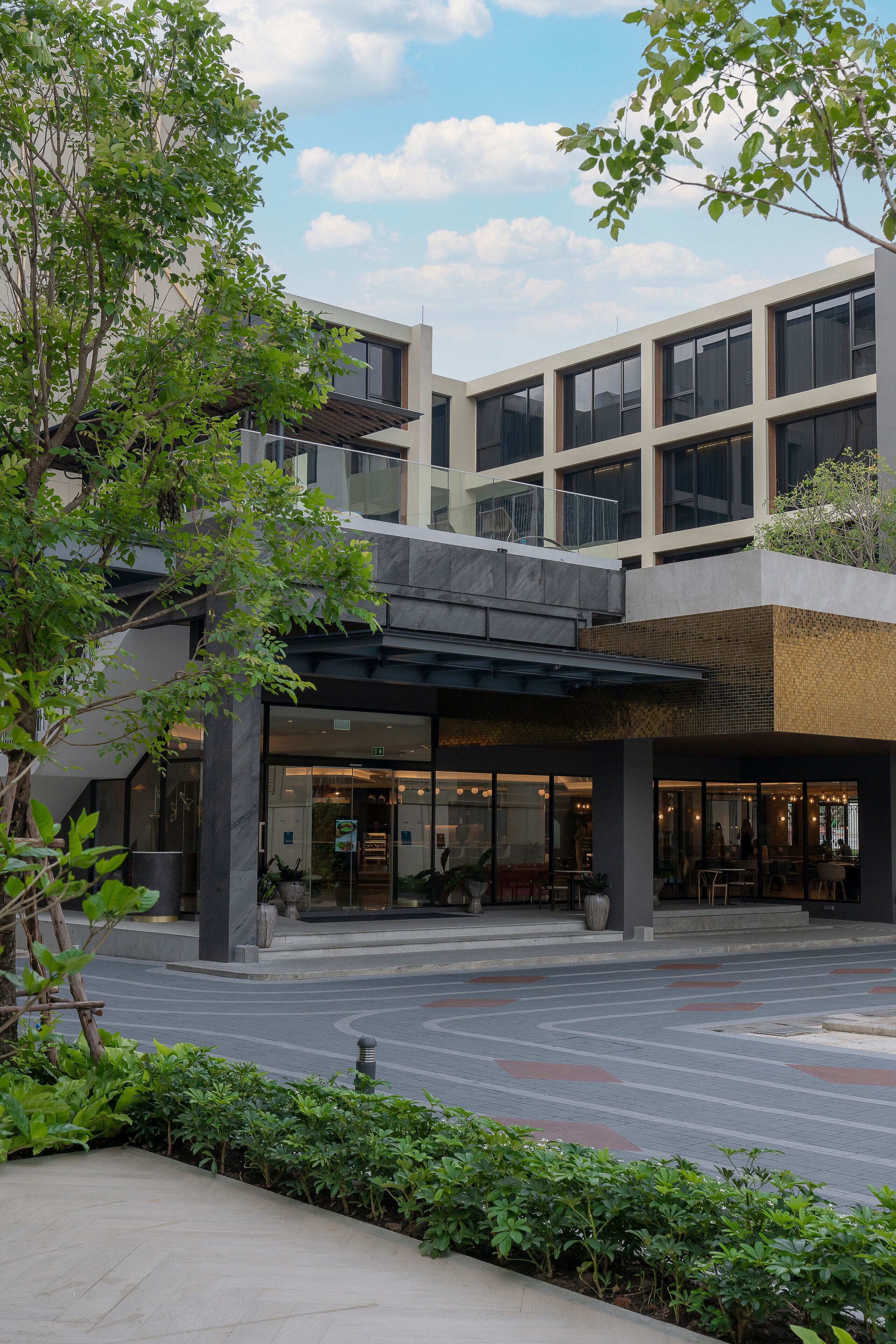 A modern building with a covered entrance, large windows, and a landscaped area with plants.