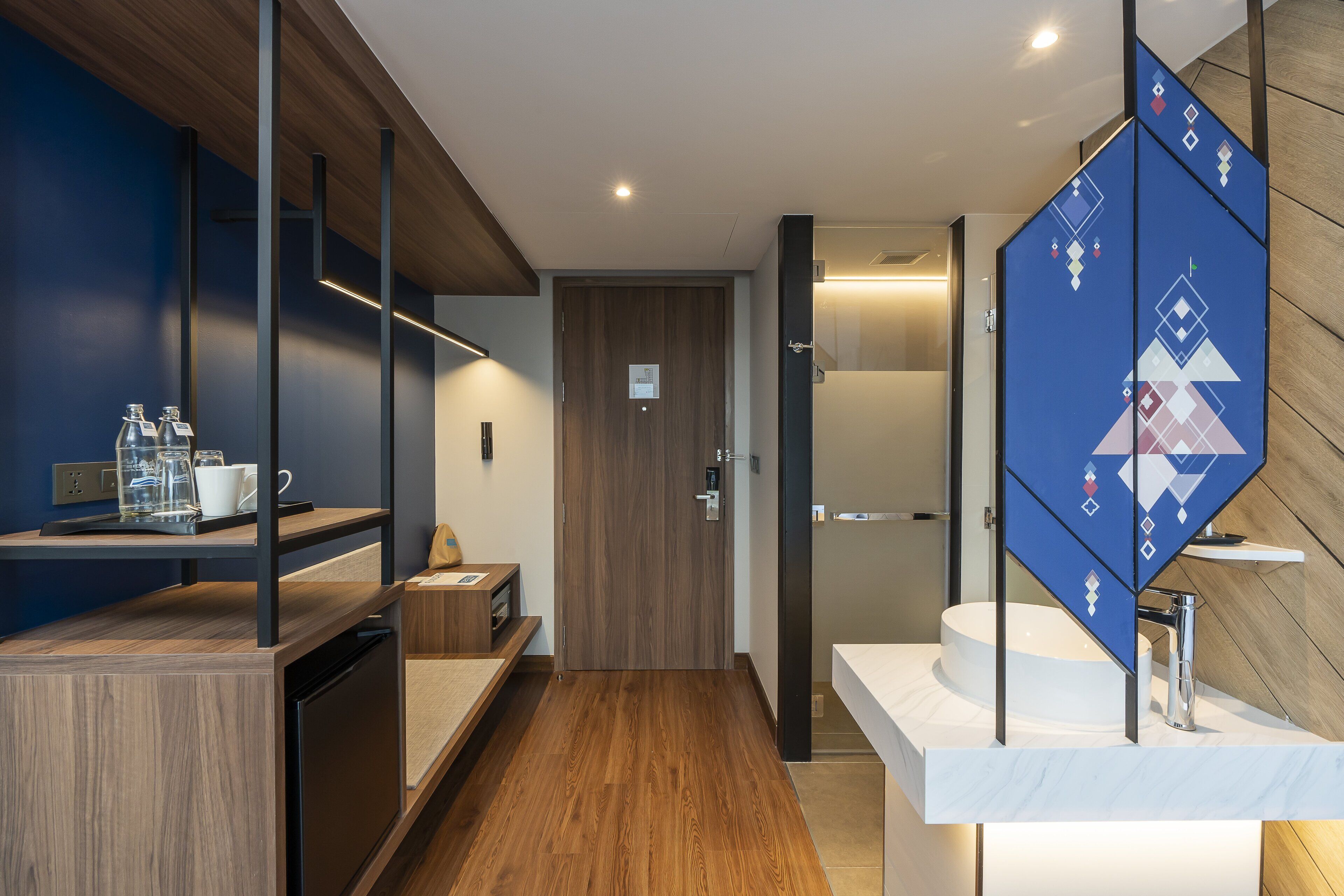 Une salle de bain moderne avec un plancher en bois, un lavabo blanc et une cloison en verre ornée de motifs géométriques.