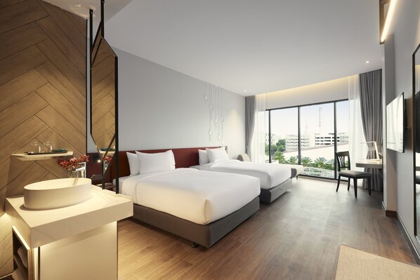Habitación de hotel moderna con dos camas, un ventanal grande con vistas a la ciudad, un escritorio y un baño con espejo y lavabo.