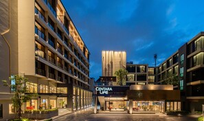 Un hotel moderno con un llamativo letrero 'Centara Life', que presenta una entrada espaciosa y una fachada bien iluminada.