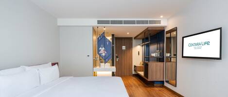 Habitación de hotel moderna con una cama grande, un armario, un espejo y un televisor que muestra el nombre del hotel.
