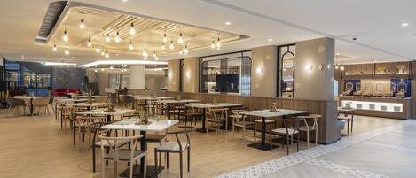 A spacious restaurant with multiple tables and chairs, a counter with a display case, and a modern ceiling design with hanging lights.