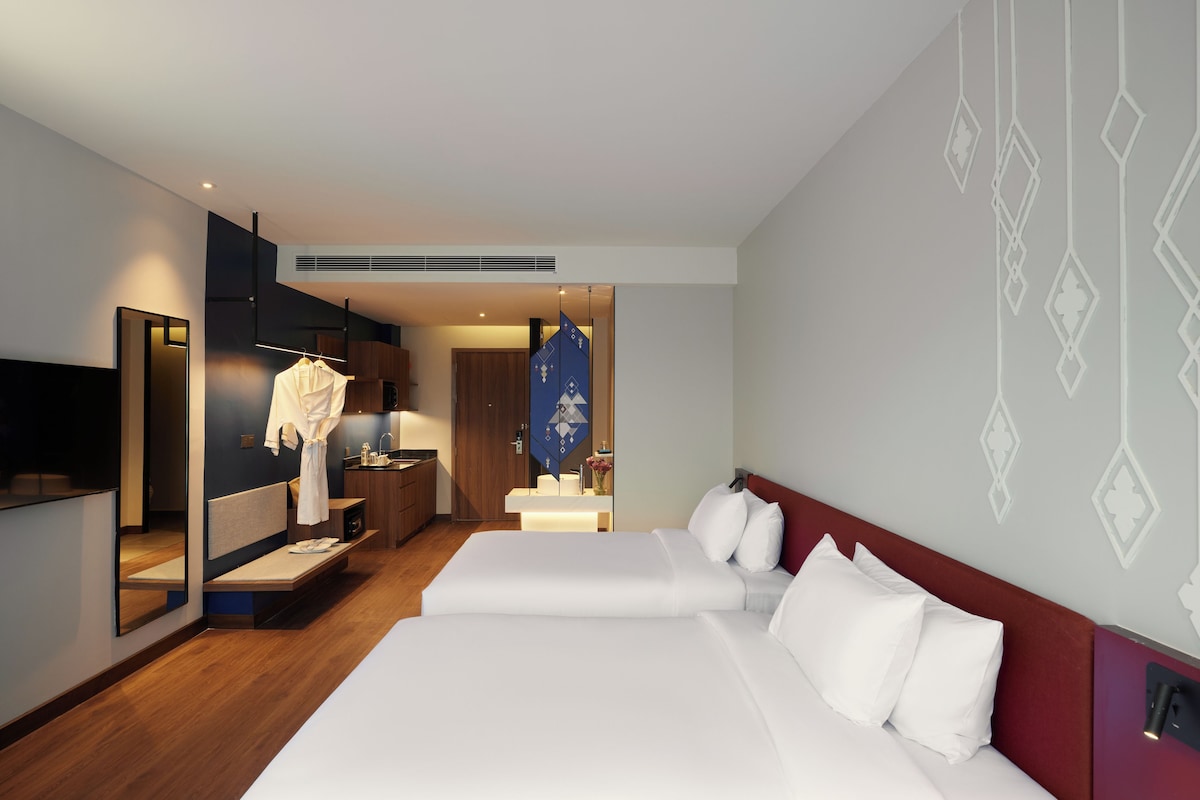 Hotellihuone, jossa on kaksi sänkyä, peili, kylpytakki sekä kylpyhuone, jossa on pesuallas ja peili.
