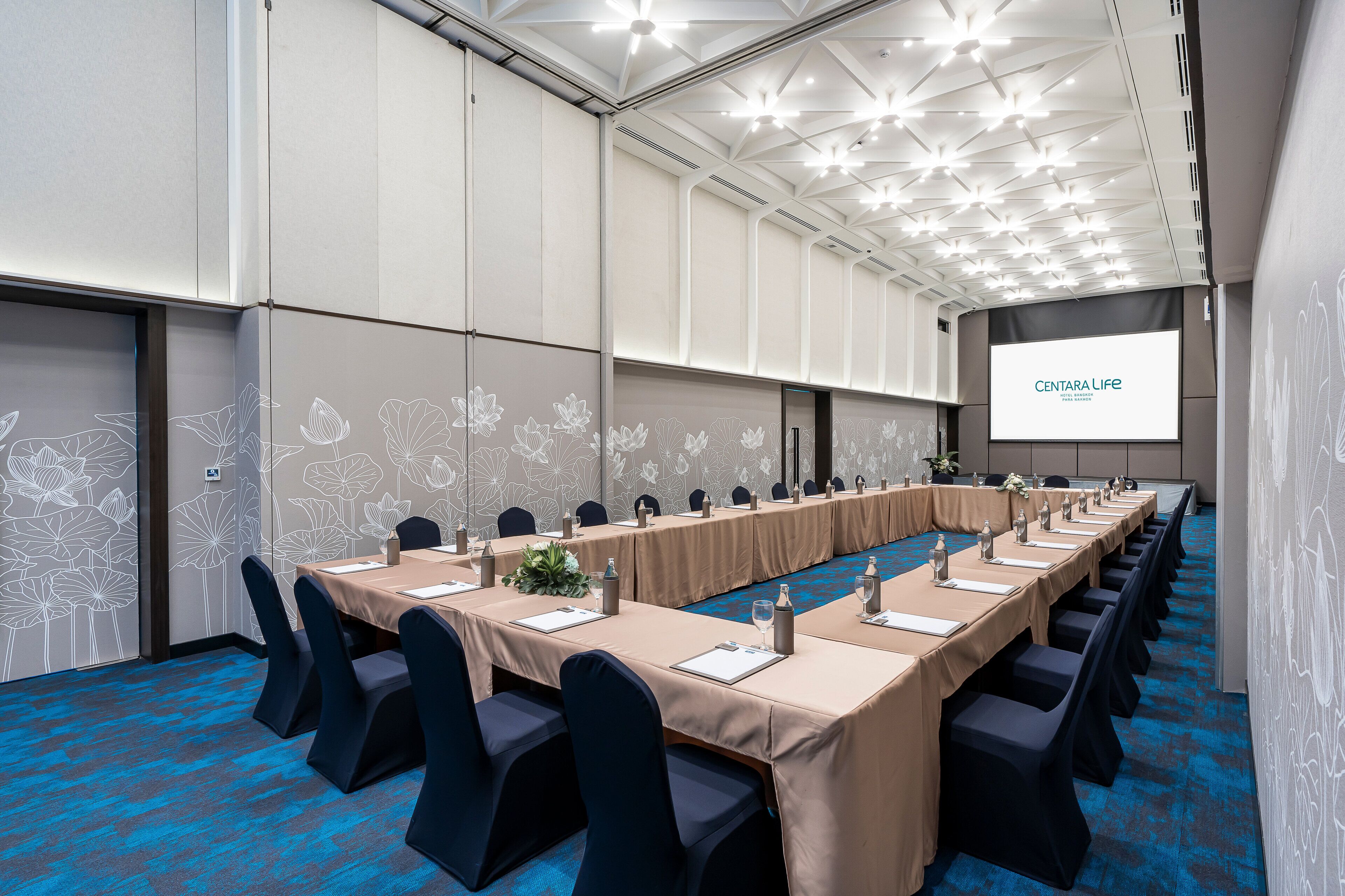 A conference room with a long table, chairs, and a screen displaying 'CENTARA LIFE'.