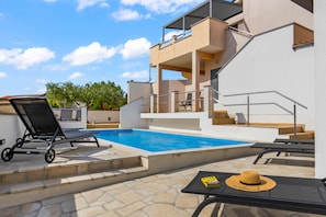 A swimming pool with lounge chairs, a table with a hat, and a staircase leading to a balcony.