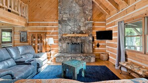 A log cabin interior with a stone fireplace, leather sofa, and a television mounted on the wall. - 🏕️  Angels Cabin, Firepit, Pool Table, LKT Mountain - Chattanooga Dwtn15 min!  (Lookout Mountain)