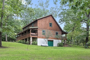 Eine Holzhütte mit Veranda, einer grünen Garagentür und einem von Bäumen umgebenen Rasen.