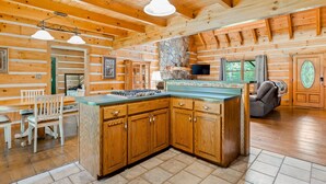 A log cabin interior with a kitchen island, wooden cabinets, and a stone fireplace. - 🏕️  Angels Cabin, Firepit, Pool Table, LKT Mountain - Chattanooga Dwtn15 min!  (Lookout Mountain)