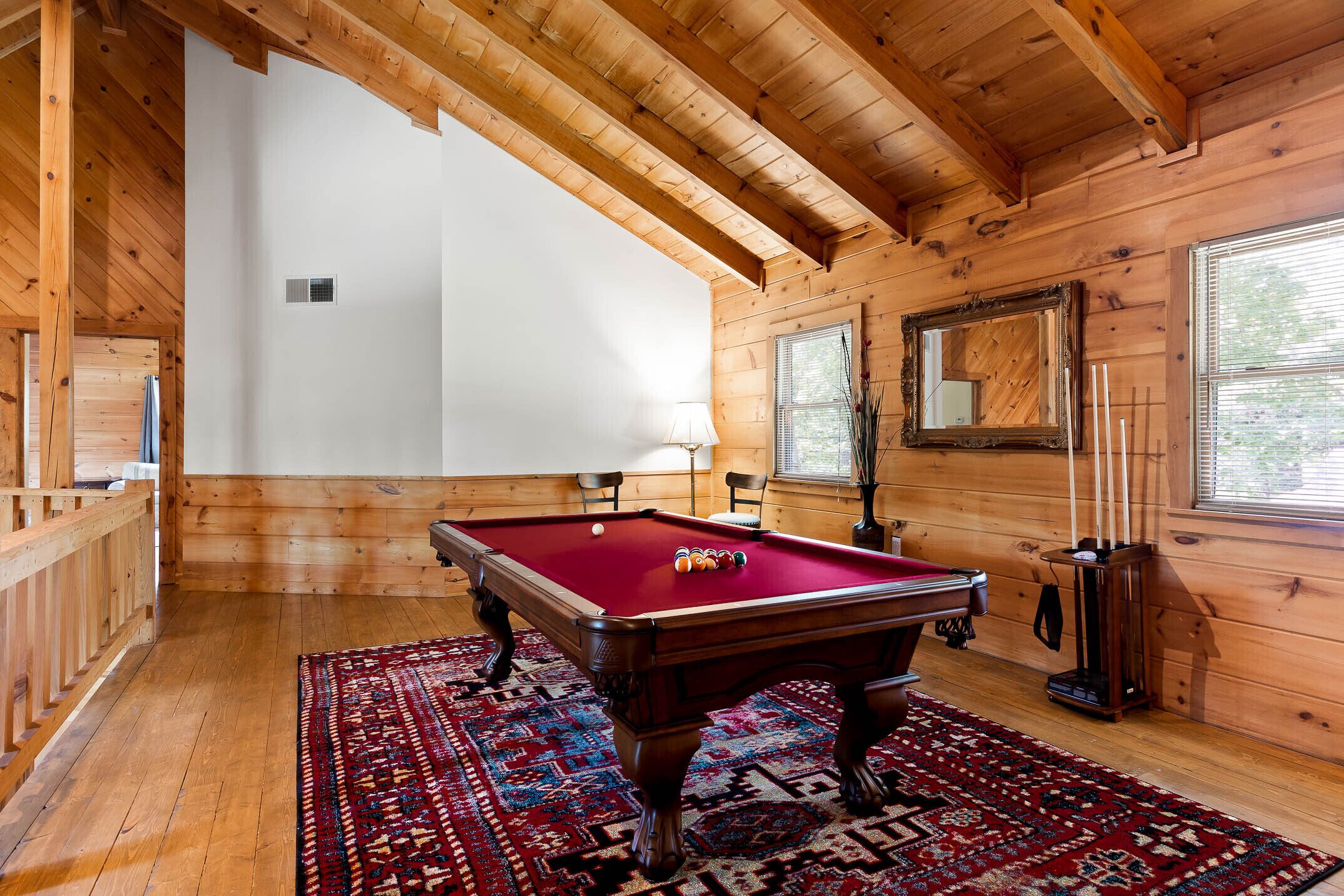 A wooden room with a pool table, a patterned rug, and a large mirror.