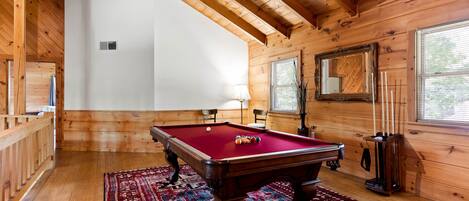 A wooden room with a pool table, a patterned rug, and a large mirror.