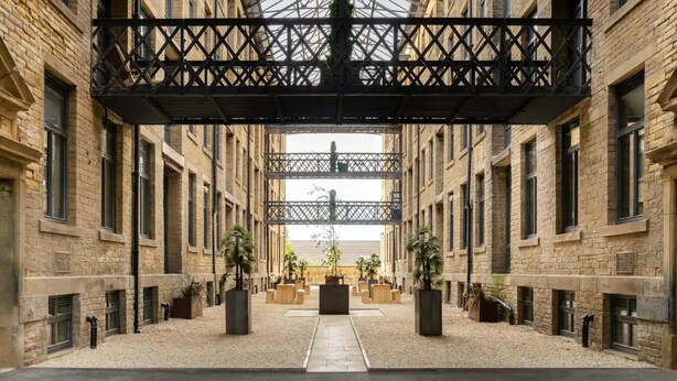 A courtyard with a central pathway, surrounded by brick buildings with large windows and a metal structure overhead. - Luxury 1-bed Apartment Bradford Free Parking (Bradford)