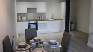 A modern kitchen with white cabinets, a black column, and a dining area with a glass table set for four. - Luxury 1-bed Apartment Bradford Free Parking (Bradford)