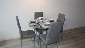 A round dining table with four chairs, each with a quilted backrest. The table is set with plates, bowls, and cups. - Luxury 1-bed Apartment Bradford Free Parking (Bradford)