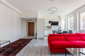 A modern living room with a red sofa, a glass coffee table, and a patterned rug. - Cozy and bright 66sqm apartment located on the 6th floor of a building with lift (with a flight of stairs at the entrance to reach it).The accommodation is located in an exceptional position, just 300m from P.zza Gae Aulenti, famous for the wonderful vie (Milano)