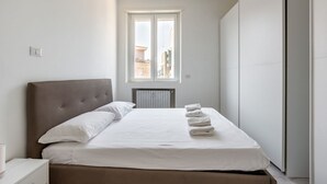 A bedroom with a bed, a nightstand, a window, and a radiator. - Cozy and bright 66sqm apartment located on the 6th floor of a building with lift (with a flight of stairs at the entrance to reach it).The accommodation is located in an exceptional position, just 300m from P.zza Gae Aulenti, famous for the wonderful vie (Milano)