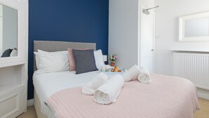 Een net opgemaakt bed met witte beddengoed, een blauwe accentmuur en een witte deur met spiegel.