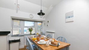 Een moderne keuken met een houten tafel, stoelen en uitzicht op de zee door grote ramen.