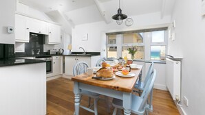Een moderne keuken met witte kastjes, een houten eettafel en uitzicht naar buiten.
