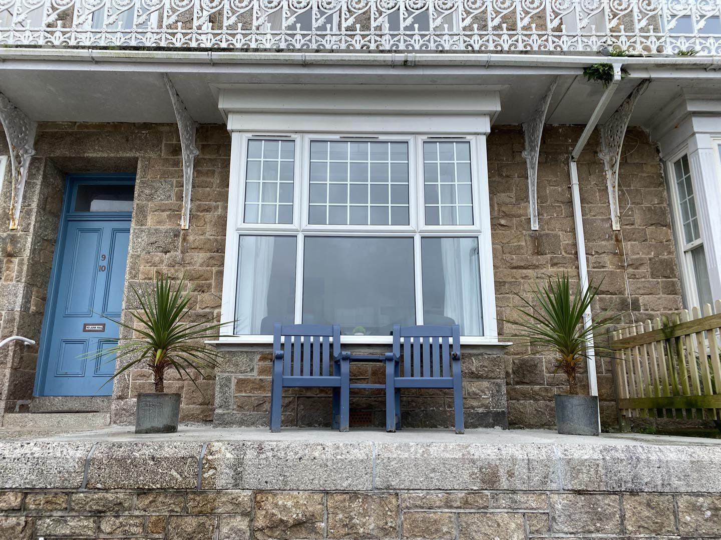 Un bâtiment en pierre avec une fenêtre blanche, une porte bleue et deux chaises bleues sur le porche avant.