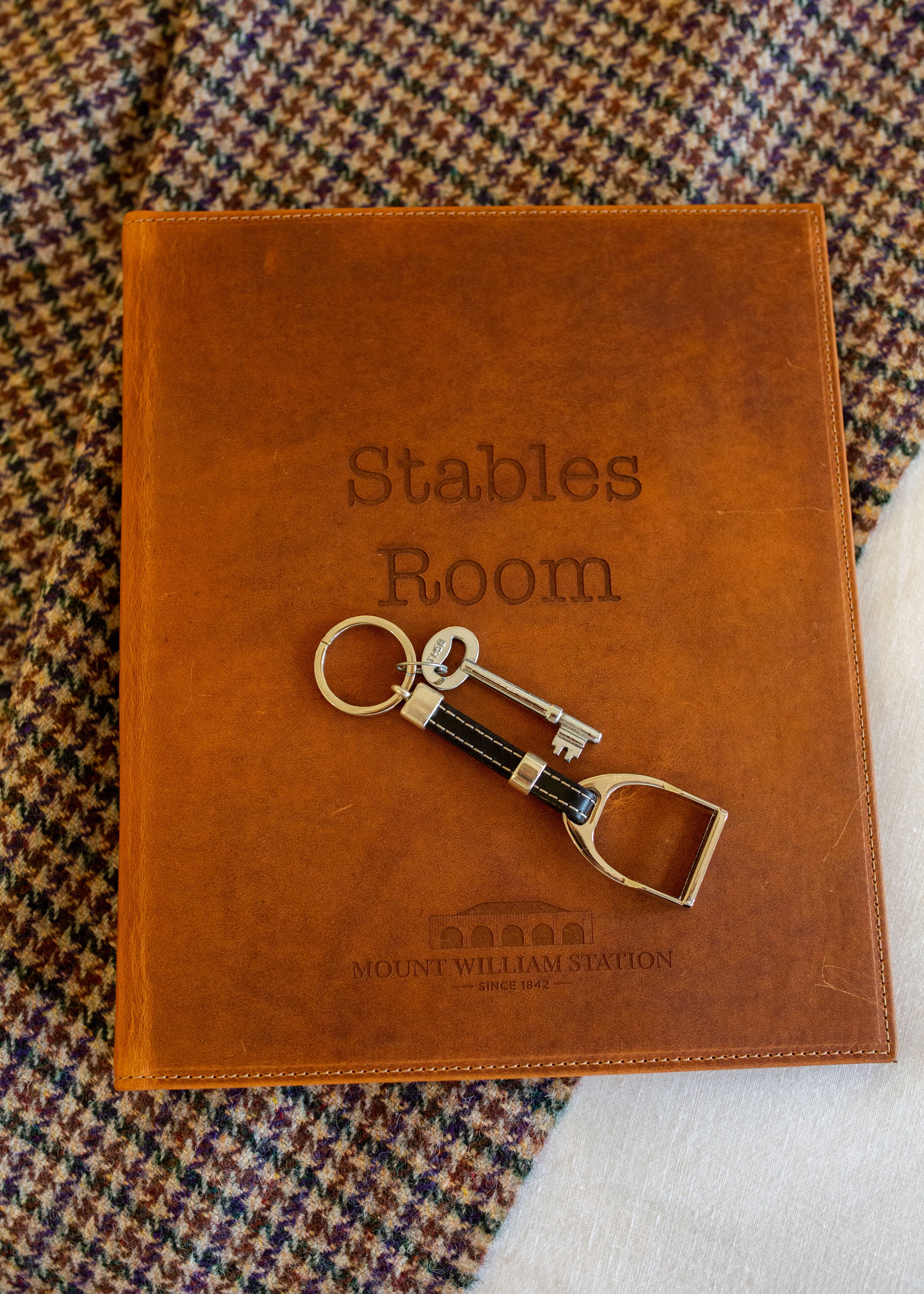 A brown leather-bound book titled "Stables Room" with a keychain on top.